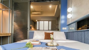 Ett hotellrum med en säng, ett nattduksbord, ett fönster och utsikt över hotellets inre.