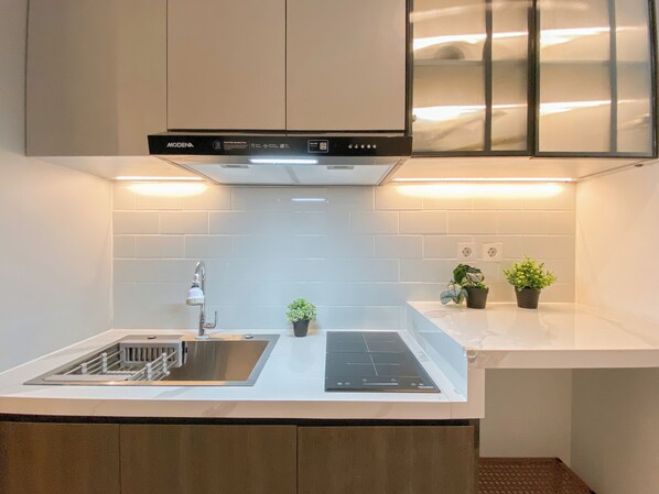 Una cocina moderna con armarios blancos, un lavamanos de acero inoxidable, una estufa empotrada y dos plantas en la encimera.