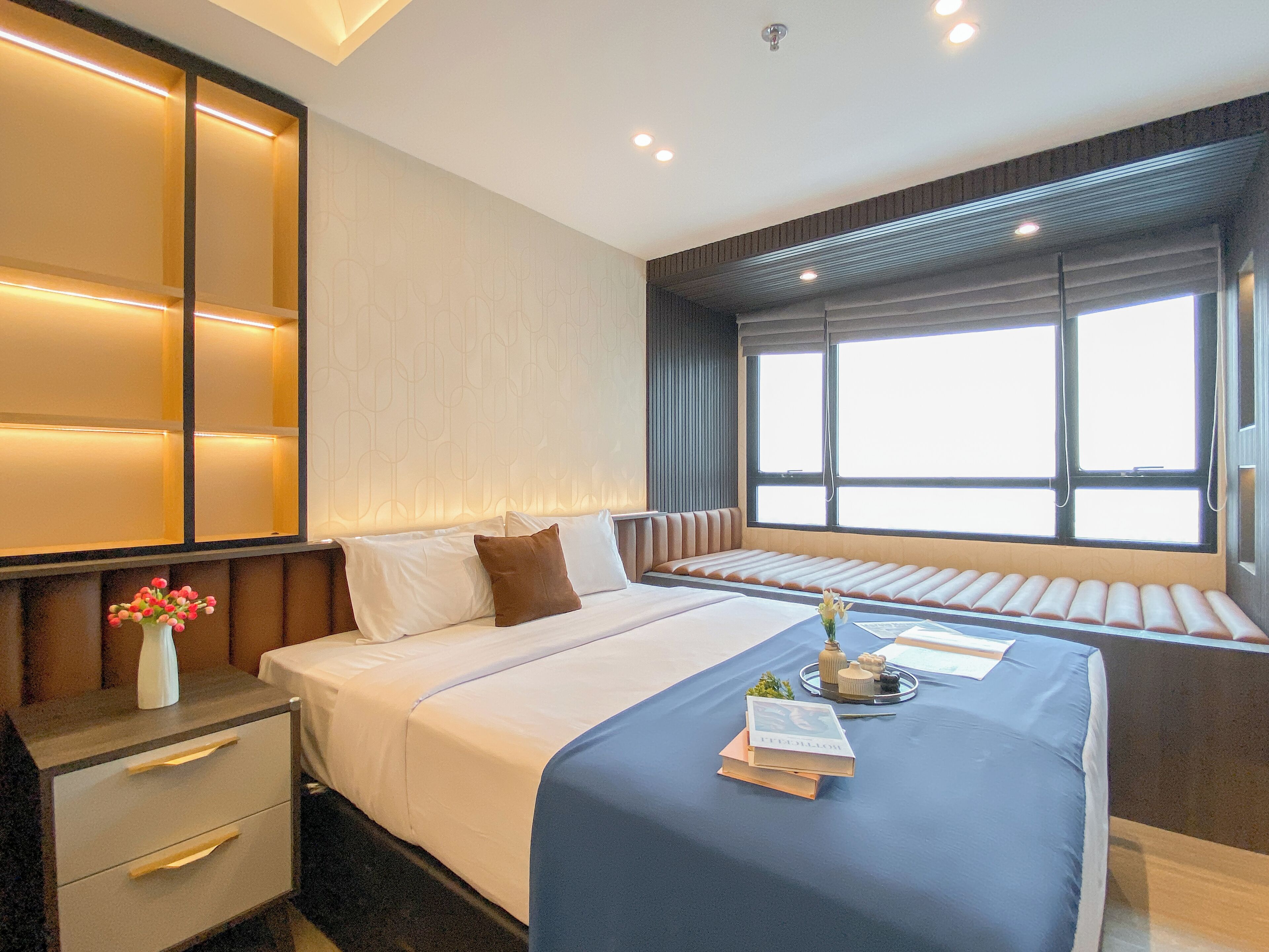 Una habitación de hotel moderna con una cama grande, mesitas de noche, un asiento junto a la ventana y un jarrón con flores.