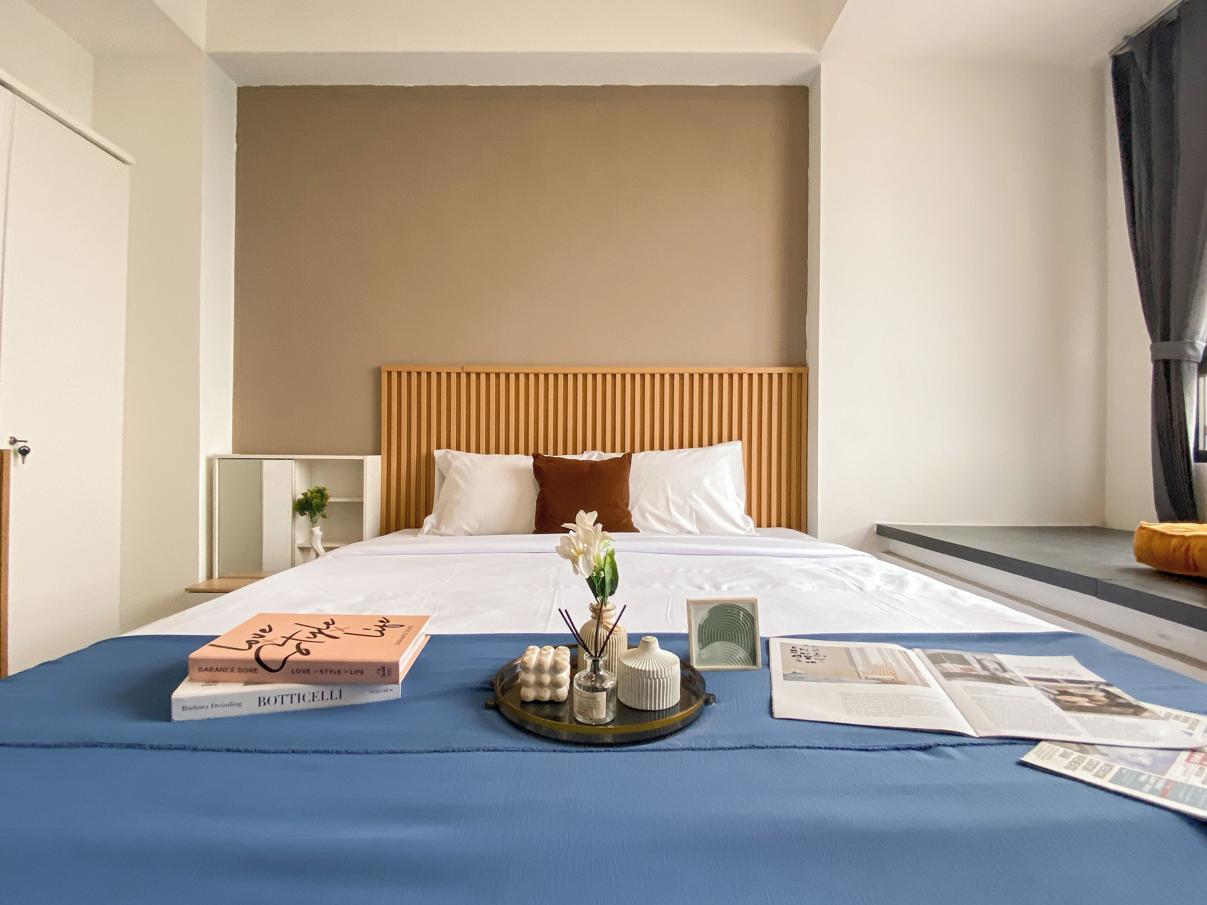 A hotel room with a bed, a bedside table, a tray with books and a vase of flowers.