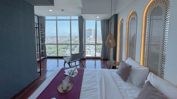 A modern hotel room with a large window, a bed, a chair, and a small table. - 1Br Near Uinsa At Tamansari Papilio Apartment (Surabaya)