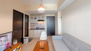 A modern living room with a grey sofa, a wooden coffee table, and a TV on a wooden stand. - 1Br Near Uinsa At Tamansari Papilio Apartment (Surabaya)