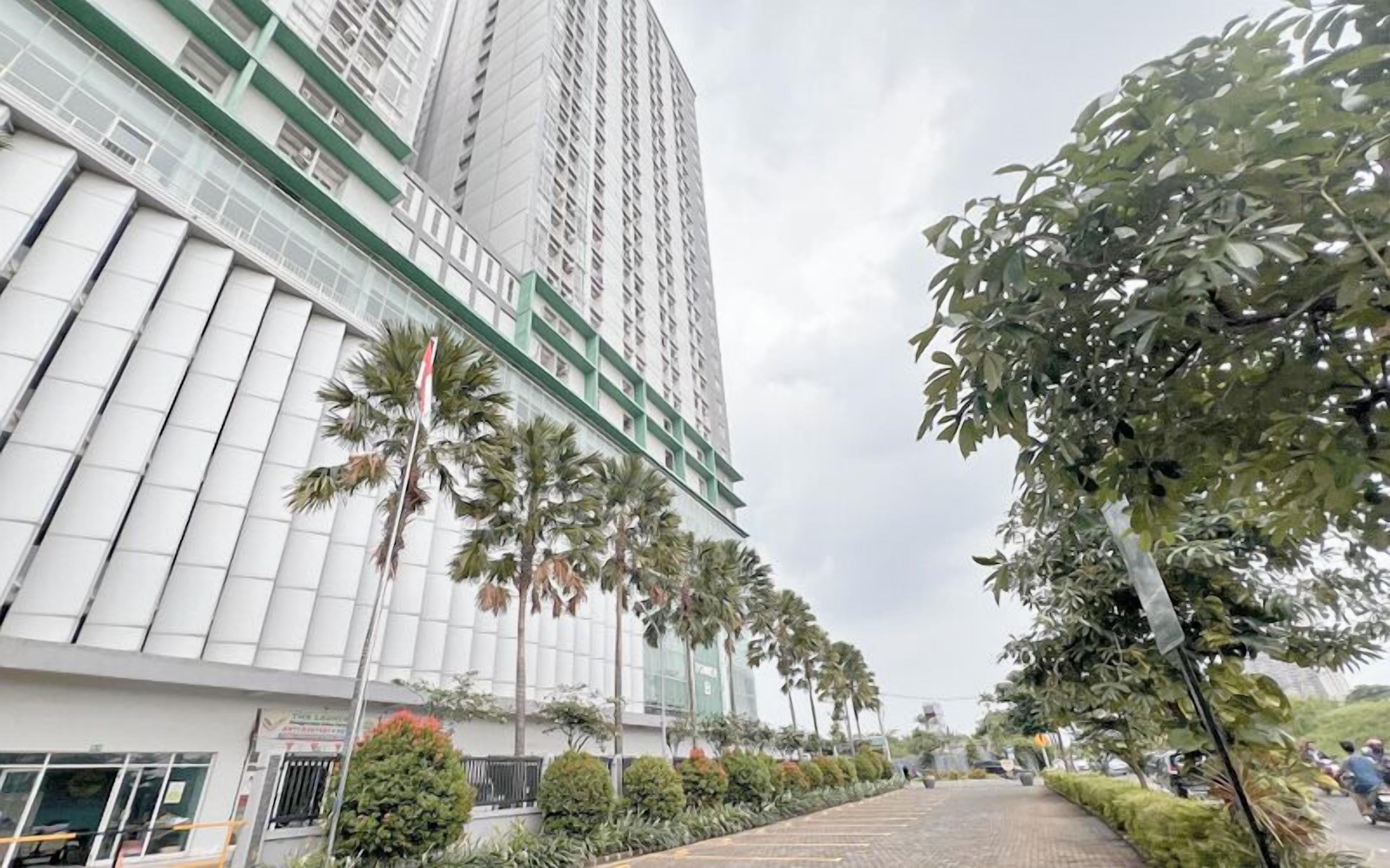 Un moderno edificio de gran altura con fachada de vidrio, palmeras y un sendero pavimentado.