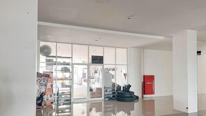 Un hall d’entrée spacieux avec une porte vitrée donnant sur une zone commerciale, une extincteur rouge et une poubelle noire.