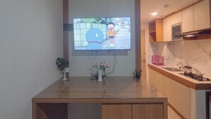 Une cuisine avec un téléviseur fixé au mur diffusant un dessin animé, une petite plante en pot et un vase rempli de fleurs posé sur le comptoir.