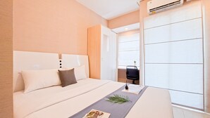 A hotel room with a bed, a desk, and an air conditioning unit. - Warm Studio At Serpong Garden Apartment (Cisauk)