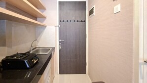 A compact kitchen with a built-in sink, a black portable stove, and a door with a key lock. - Warm Studio At Serpong Garden Apartment (Cisauk)