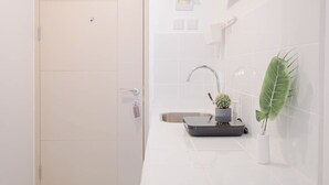 Un baño moderno con pared de azulejos blancos, un lavabo con grifo, una pequeña planta de cactus y una decoración de hoja verde grande.