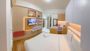 A hotel room with a bed, a TV, a bathroom, and a small kitchenette. - Pure Nest Studio At Candiland Apartment (Semarang)
