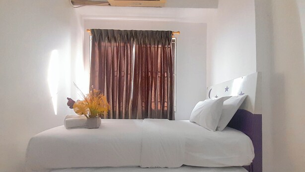 A neatly made bed with white linens, a bedside table with a vase of flowers, and a window with curtains. - 1Br Near Gedebage Station At Tamansari Panoramic Apartment (Bandung)