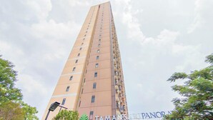 A high-rise building with multiple floors and balconies, surrounded by trees and a partly cloudy sky. - 1Br Near Gedebage Station At Tamansari Panoramic Apartment (Bandung)