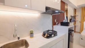 A modern kitchen with a stainless steel sink, a small potted cactus, a portable gas stove, and a built-in range hood. - Marble Haven Studio At Tokyo Riverside Pik 2 Apartment (Teluknaga)