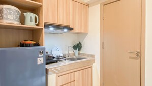 A compact kitchen with a refrigerator, a kettle, a coffee maker, and a sink. - Warm Minimalist Studio Apartment Near Paramadina University At Meikarta (Cikarang)