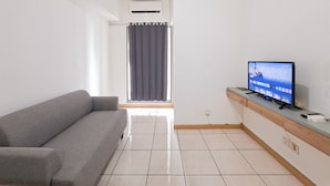 Un salon moderne avec un canapé gris, un téléviseur à écran plat posé sur une console en bois et une fenêtre avec des rideaux.