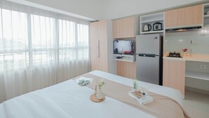 A modern hotel room with a bed, a small kitchenette, a TV, and a large window with sheer curtains. - Basic Studio Apartment At Springlake Summarecon Bekasi (Bekasi)