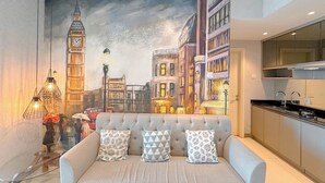 A modern living room with a large painting of a cityscape, a sofa with patterned cushions, and a glass coffee table. - Modern And Stunning 2Br At Anderson Supermall Mansion Apartment (Surabaya)