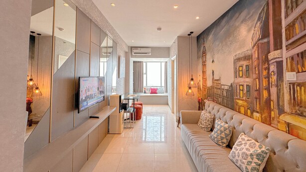 A modern living room with a sofa, a TV, and a mural on the wall. - Modern And Stunning 2Br At Anderson Supermall Mansion Apartment (Surabaya)
