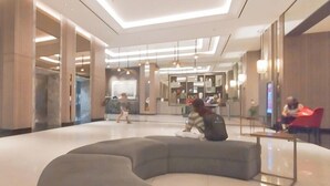 A spacious lobby with a curved seating area, a reception desk, and a large mirror reflecting the interior. - Modern And Stunning 2Br At Anderson Supermall Mansion Apartment (Surabaya)