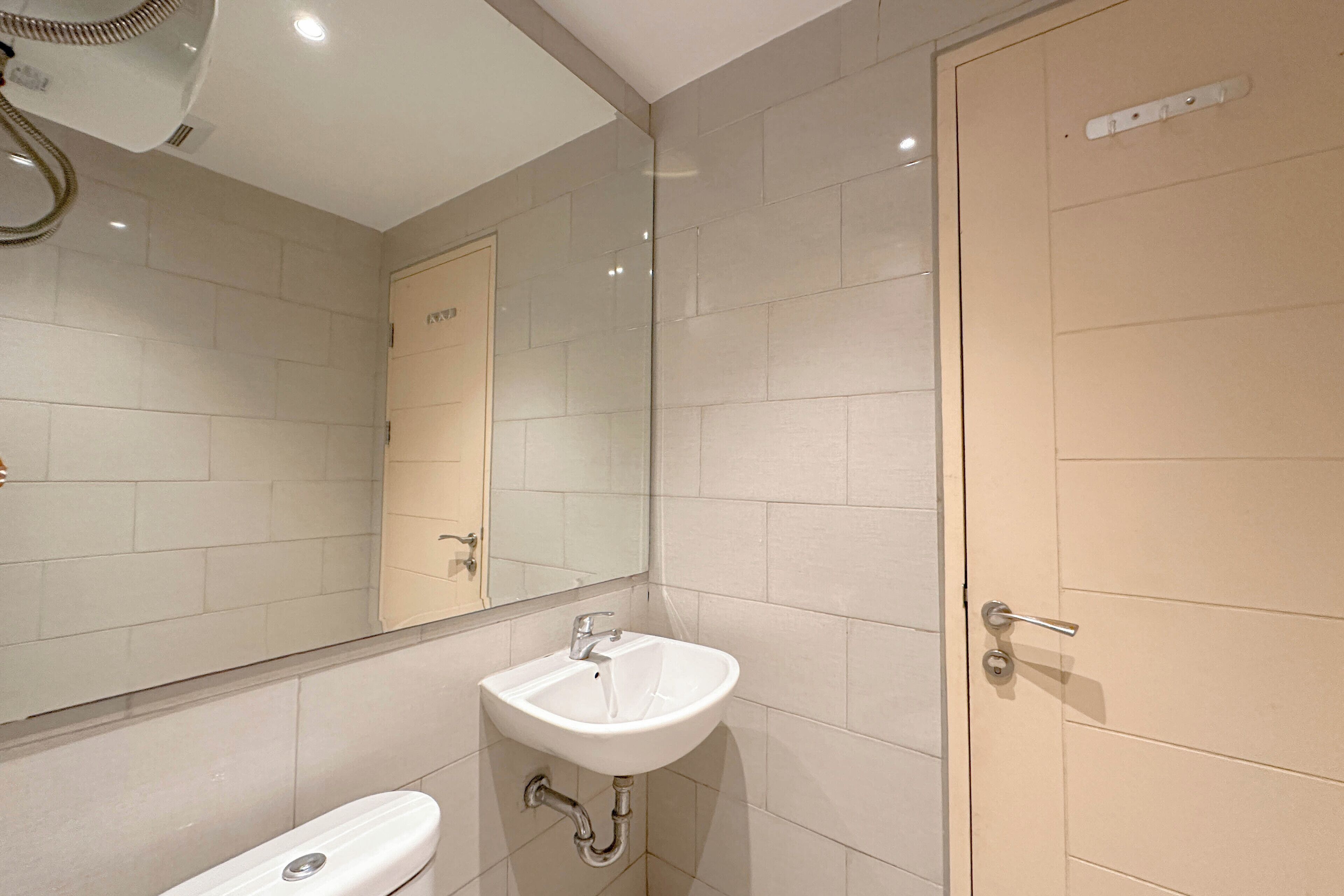 Un baño con lavamanos blanco, espejo y azulejos color beige.