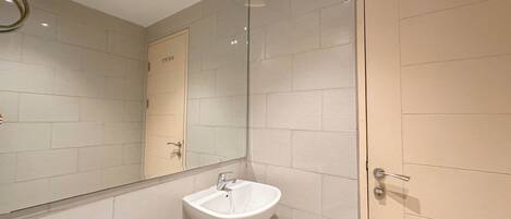Un baño con lavamanos blanco, espejo y azulejos color beige.