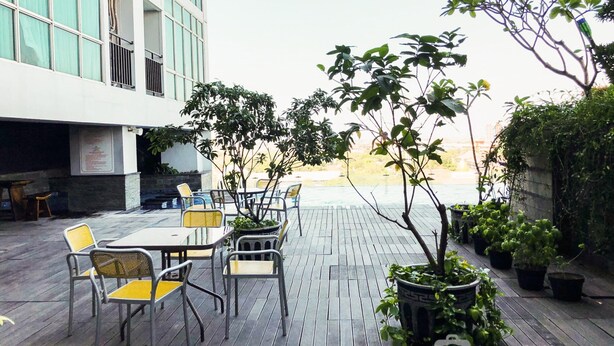 Una terrazza esterna con tavoli e sedie, circondata da piante in vaso e con vista su un edificio.