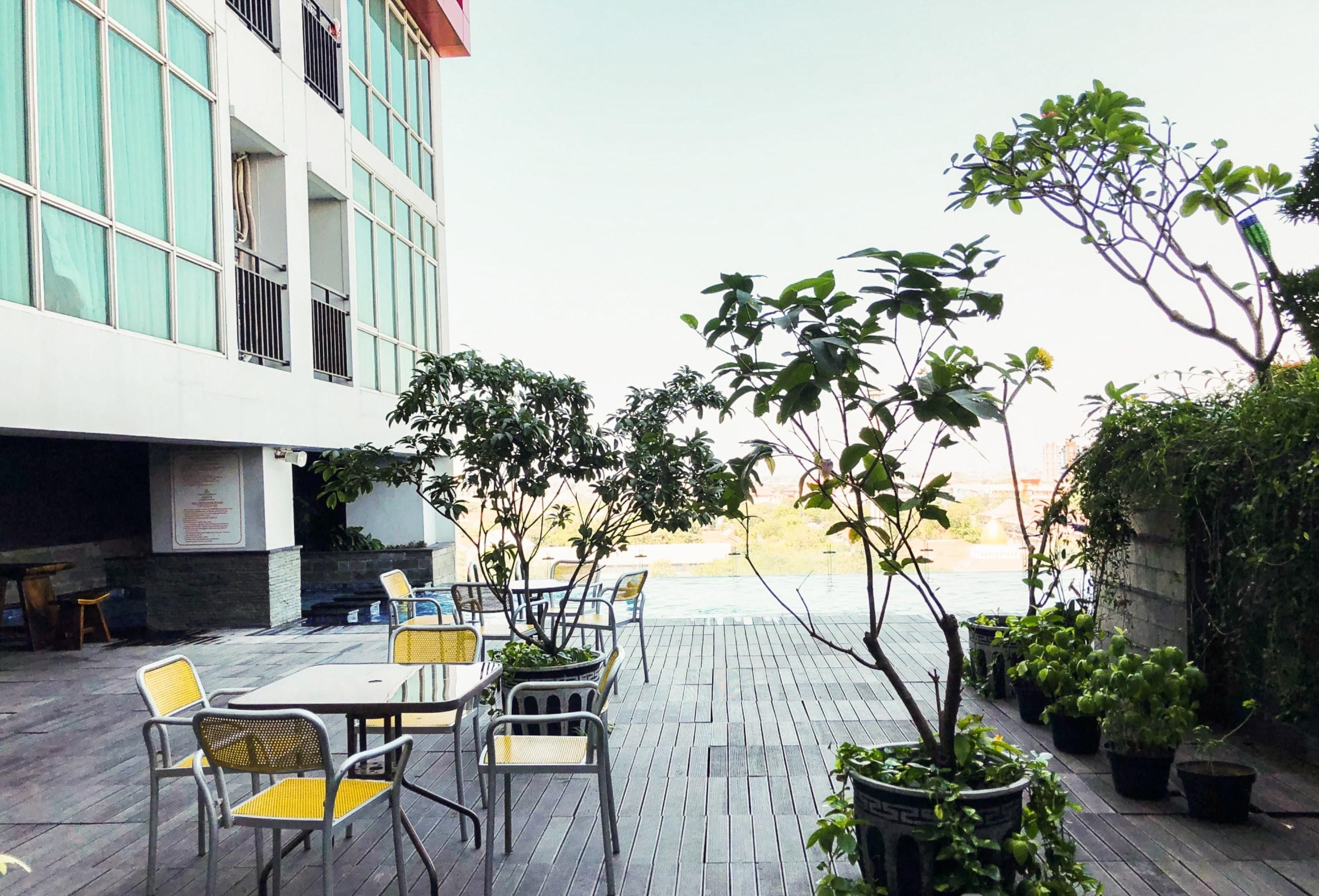 An outdoor patio with tables and chairs, surrounded by potted plants and a view of a building.