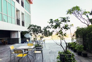 An outdoor patio with tables and chairs, surrounded by potted plants and a view of a building. - Minimalist Studio (No Kitchen) At Tamansari Papilio Apartment (Surabaya)