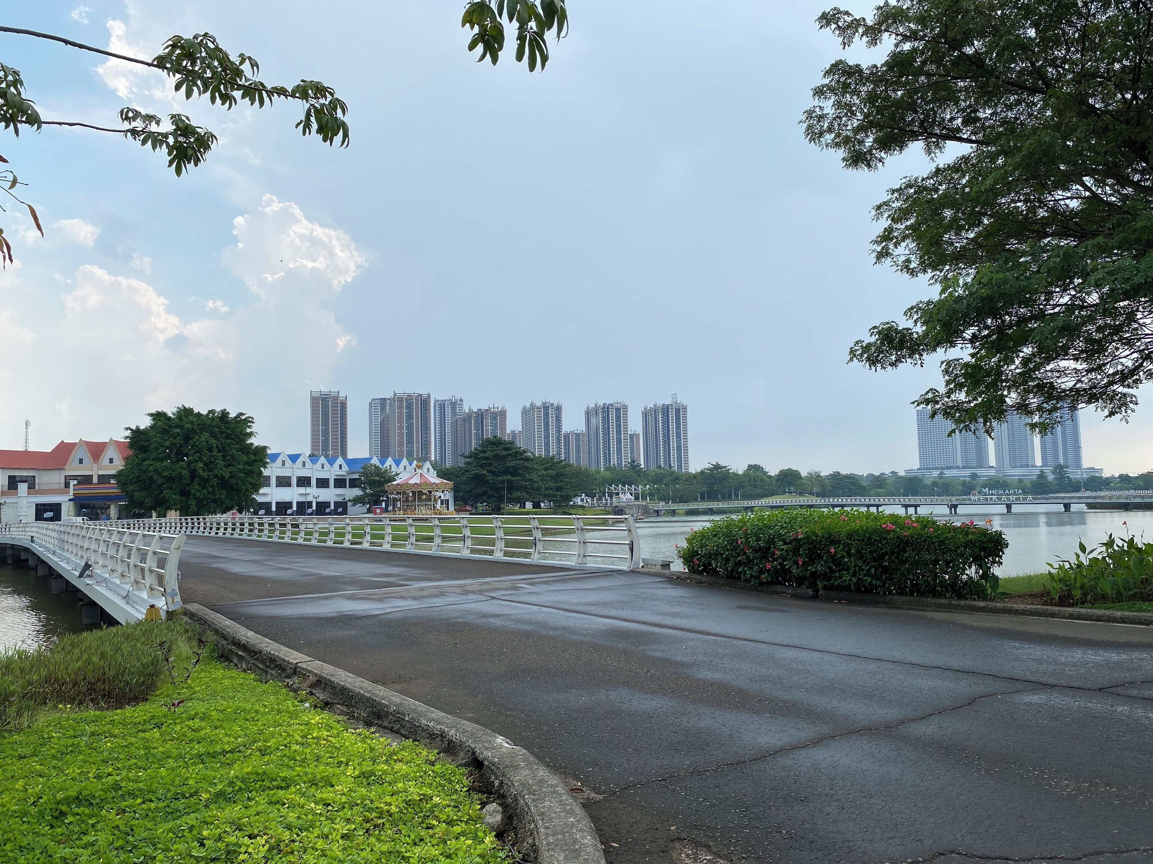 A bridge with a white railing, a body of water, and buildings in the background.