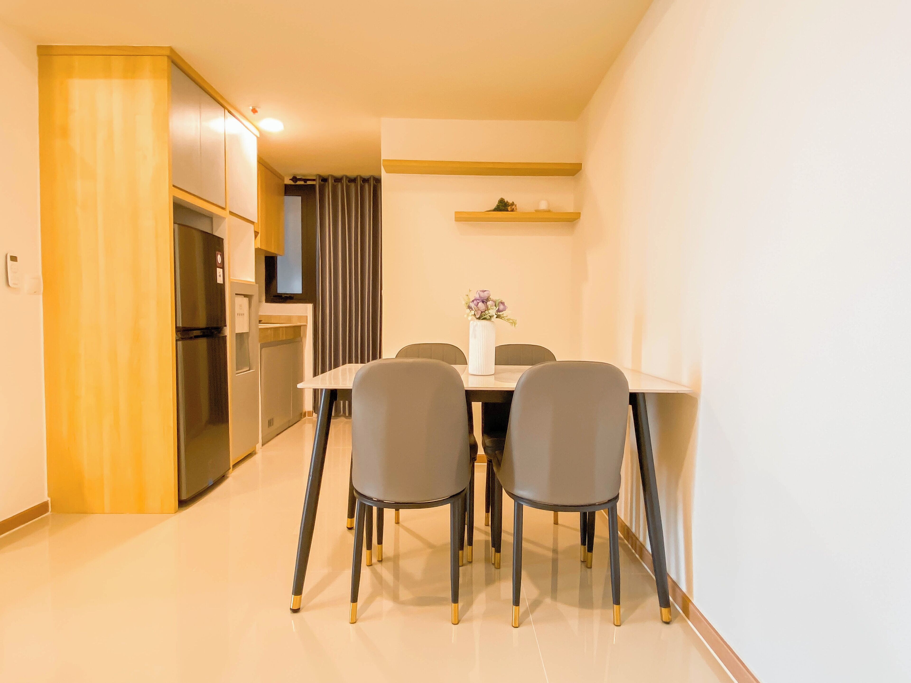Una cocina moderna con un refrigerador empotrado, una mesa de comedor con cuatro sillas y un estante pequeño encima de la mesa.
