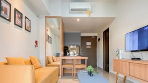 A modern living room with a sofa, a coffee table, a TV, and a dining area. - 1Br Apartment Near President University At Mustika Golf Residence (Cikarang)