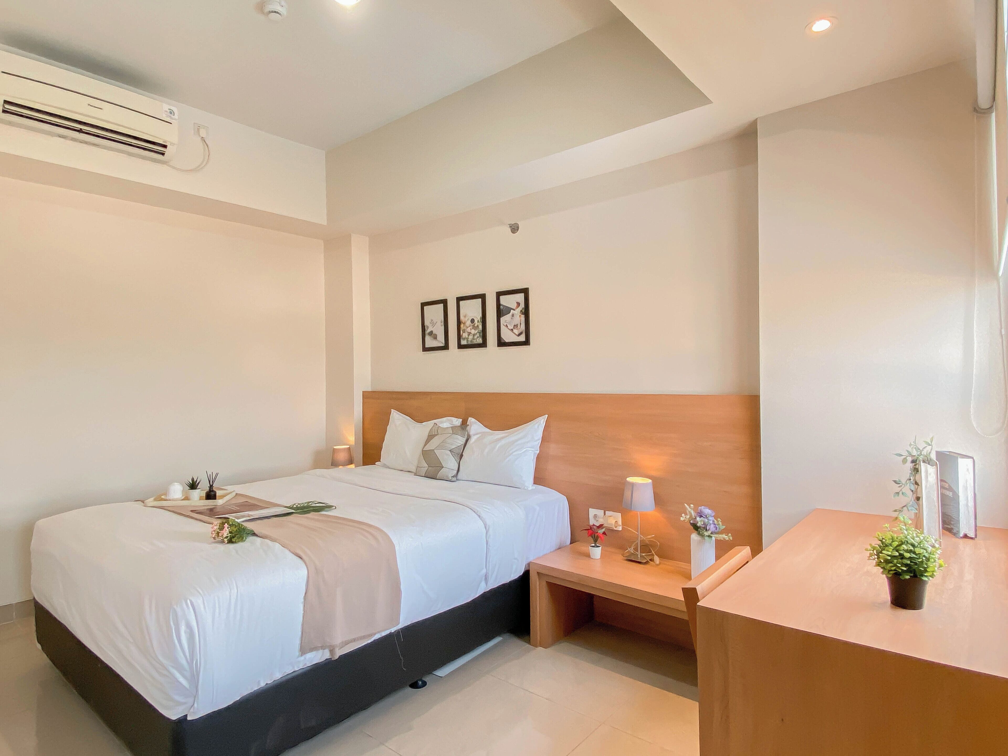 A modern hotel room with a bed, bedside table, lamp, and a small potted plant.