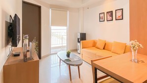 A modern living room with a sofa, coffee table, and a TV mounted on the wall. - 1Br Apartment Near President University At Mustika Golf Residence (Cikarang)