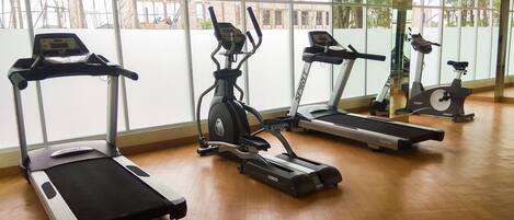A gym with four treadmills, large windows, and a wooden floor.