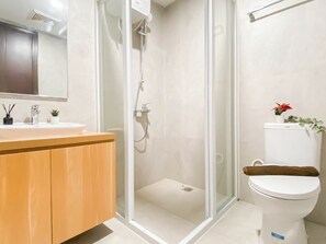 A modern bathroom with a glass-enclosed shower, a wooden vanity, a white sink, and a toilet with a brown seat.