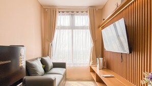 A modern living room with a flat-screen TV mounted on a wooden wall, a sofa, a coffee table, and a TV stand with a remote control. - 2Br At Apartment Pollux Chadstone Cikarang (Cikarang)