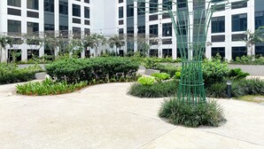 A modern building with a courtyard featuring a metal sculpture, lush greenery, and a concrete pathway. - 2Br At Apartment Pollux Chadstone Cikarang (Cikarang)