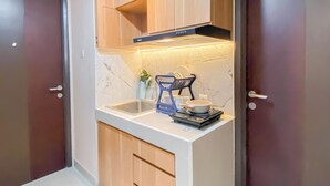 A compact kitchen with wooden cabinets, a built-in microwave, and a dish rack. - 2Br At Apartment Pollux Chadstone Cikarang (Cikarang)