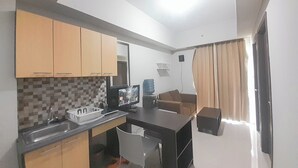 A compact kitchen with wooden cabinets, a microwave, and a small dining area with a table and chairs. - Simple Look 2Br Apartment Near Universities At Skyland City Jatinangor (Hegarmanah)