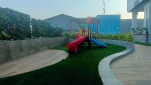 A playground with two slides and a climbing structure, surrounded by green artificial grass and concrete pathways. - Modern Looking Studio Apartment At Suncity Residence (Sidoarjo)