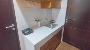 A compact kitchen with a sink, wooden cabinets, a small countertop, and a door with a handle. - Modern Looking Studio Apartment At Suncity Residence (Sidoarjo)