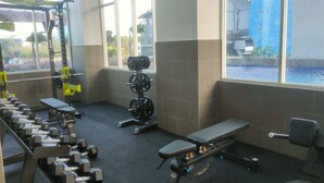 A gym with weightlifting equipment, a bench, and large windows. - Modern Looking Studio Apartment At Suncity Residence (Sidoarjo)
