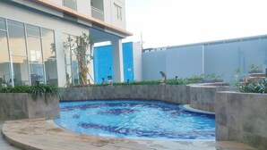 A swimming pool with a curved edge, surrounded by a low stone wall and steps leading into the water. - Modern Looking Studio Apartment At Suncity Residence (Sidoarjo)