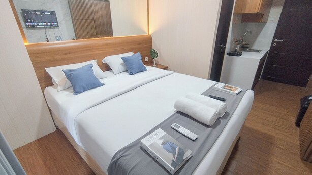A hotel room with a bed, bedside tables, a TV, and a small kitchenette. - Modern Looking Studio Apartment At Suncity Residence (Sidoarjo)