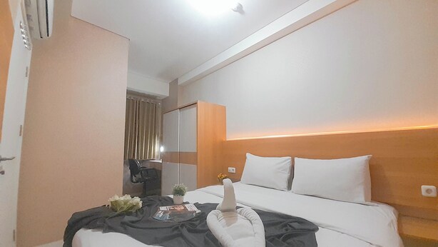 A hotel room with a bed, a bedside table, a mirror, and a window with curtains. - 2Br Near Unpar At Parahyangan Residence Apartment (Bandung)