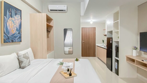 Habitación de hotel moderna con cama, kitchenette pequeña, televisor y un cuadro en la pared.