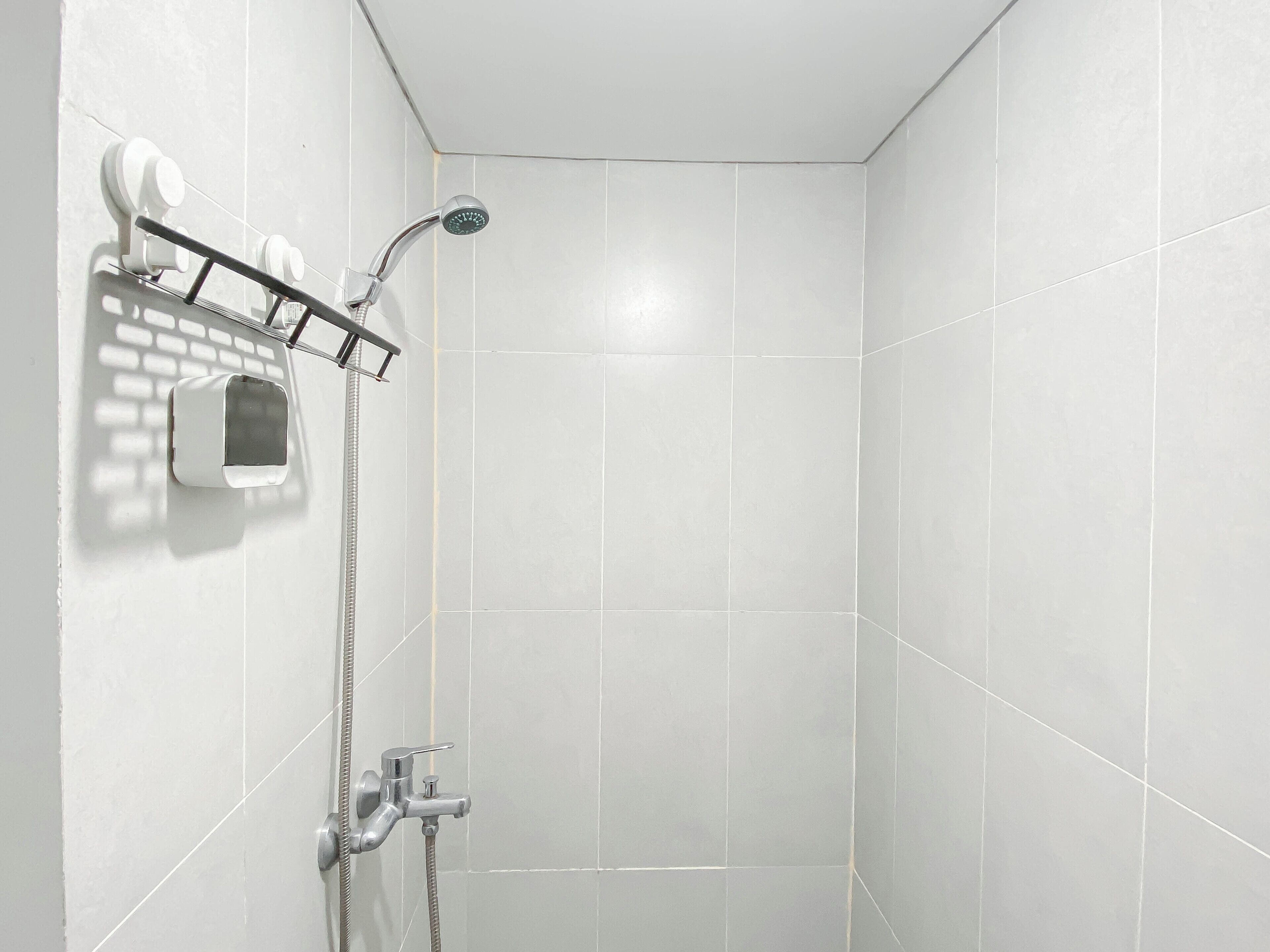Une douche équipée d’un pommeau de douche à main, d’un flexible de douche et d’un panneau de commande fixé au mur.
