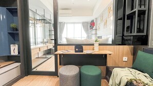 A compact, modern room with a bed, a small table with a bag and a vase, a green ottoman, and a large window with curtains. - 1Br Near Aeon Alam Sutera At Collins Boulevard Apartment (Tangerang)