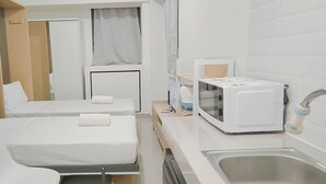 A hotel room with two beds, a microwave, a sink, and a small table with a kettle. - Basic Studio (No Kitchen) At Apartment Bandaraya - Tallasa City Makassar (Makassar)