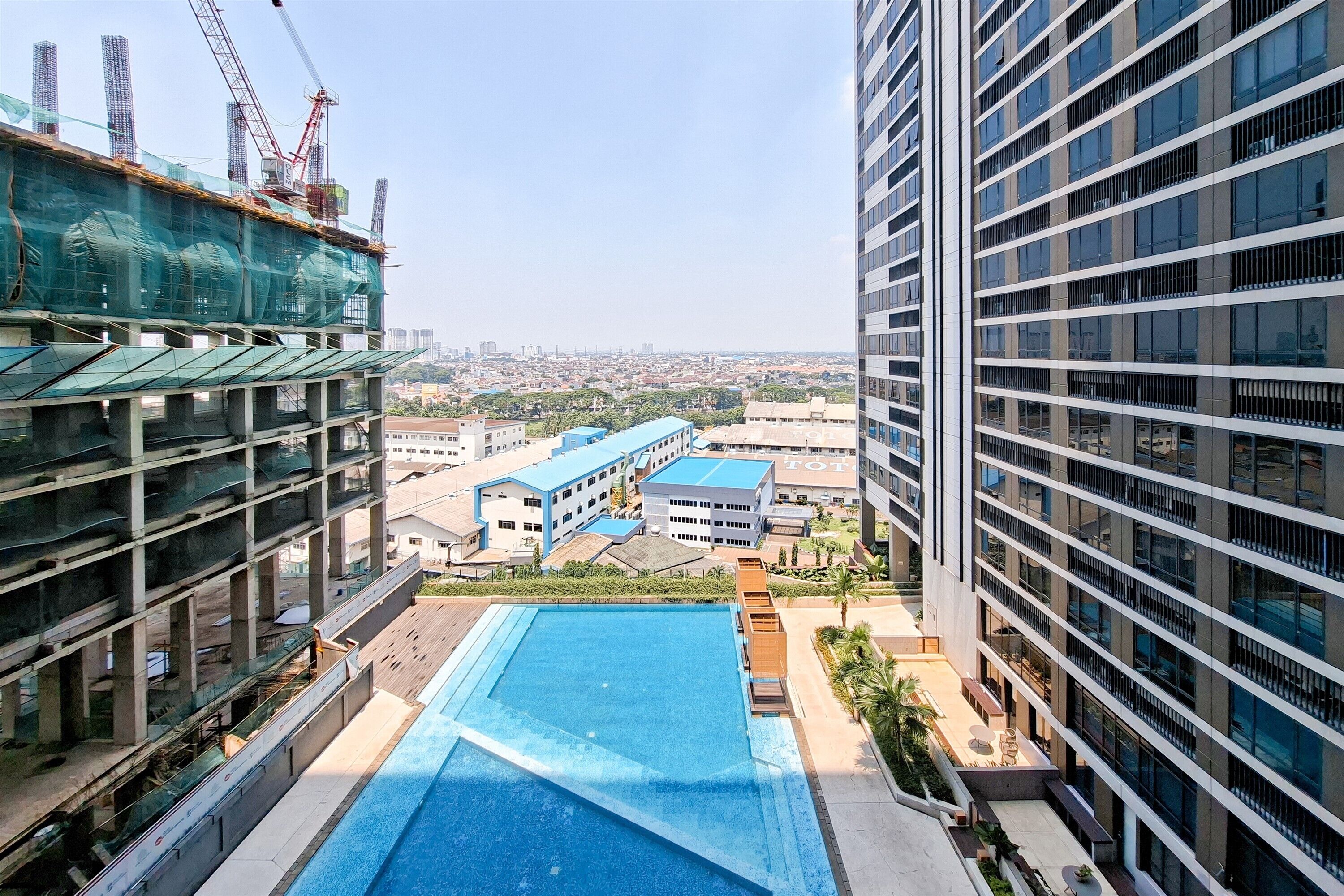 A high-rise building with a rooftop pool, surrounded by other buildings and construction cranes in the background.