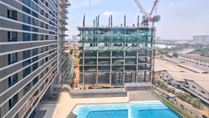 A modern building with a pool area, construction cranes, and a river in the background. - Modern Studio Near Binus Alam Sutera At Collins Boulevard Apartment (Tangerang)
